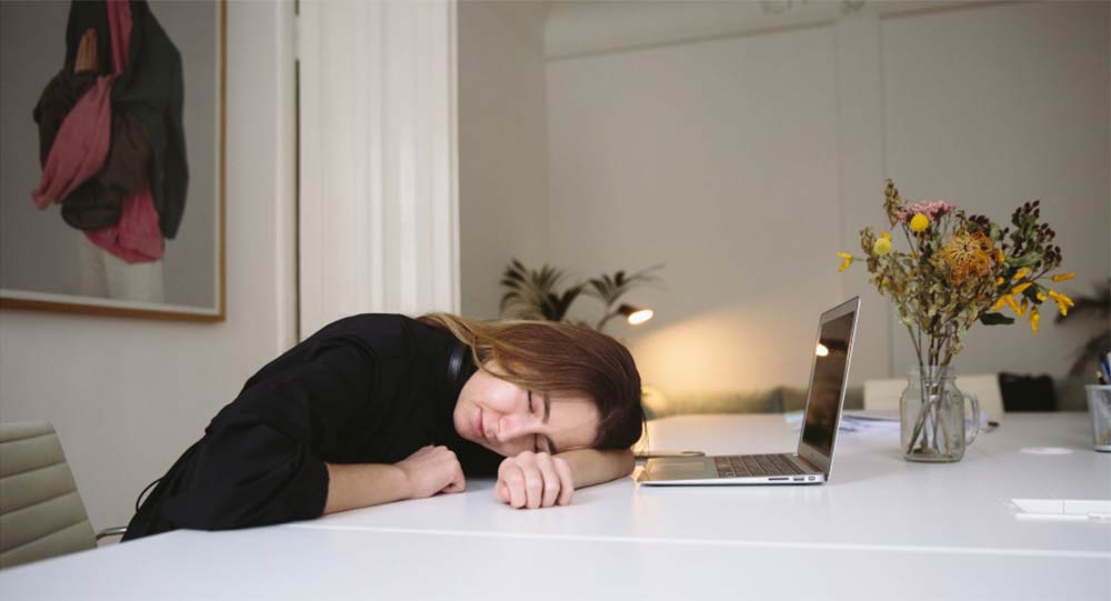 A young woman has fallen asleep at her computer while studying at the dining room table
